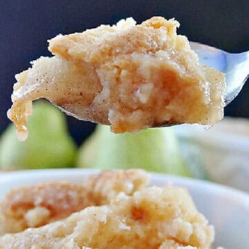 A shallow white bowl filled with pear cobbler with a scoop of vanilla ice cream on top.