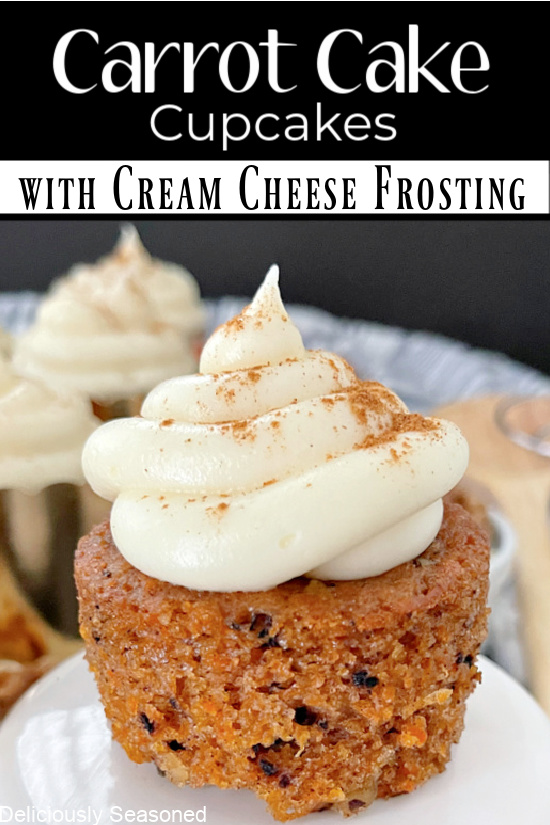 A carrot cake cupcake topped with cream cheese frosting and sprinkled with cinnamon, sitting on a white stand. 