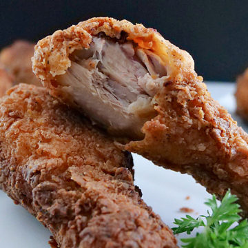 Crispy fried chicken drumsticks leaning on each other with a bite missing from one.