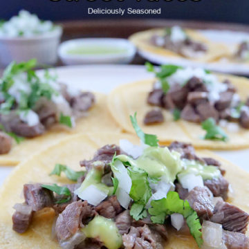 A large tray with corn tortillas laid out and beef, onion, and cilantro on top of each taco.