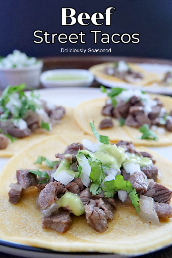 A large tray with corn tortillas laid out and beef, onion, and cilantro on top of each taco.