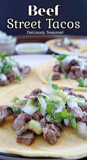 A close up photo of corn tortillas with beef, diced onion, and cilantro on top.