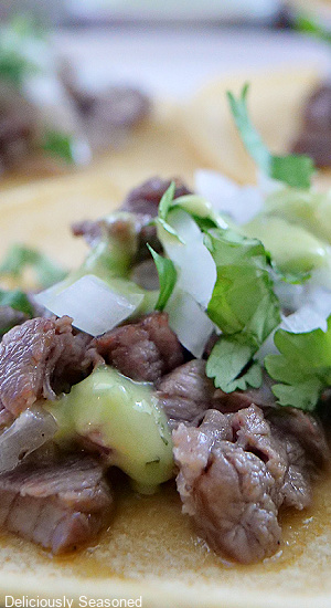 A beef street taco with cubed beef, onions, cilantro, and a green sauce on top.