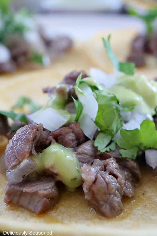 A close up photo of one taco, where you can see the diced beef, the toppings of the taco, and a creamy green sauce.