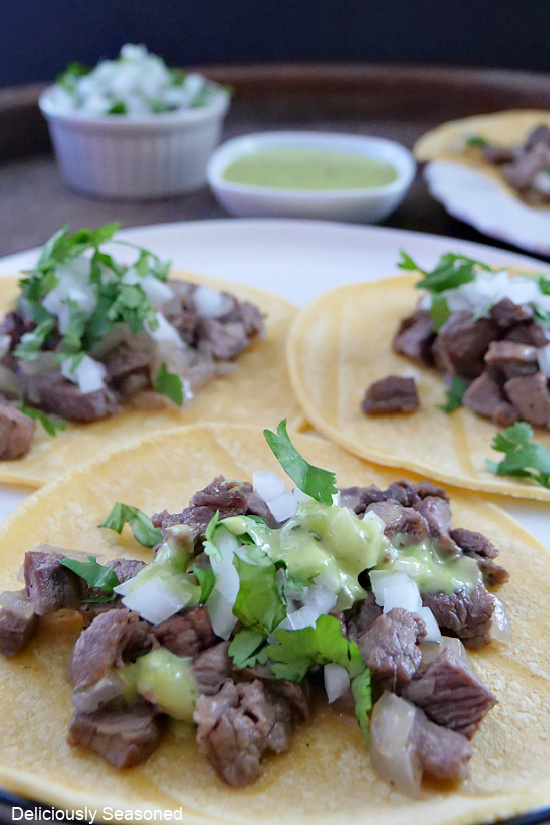 A plate lined with corn tortillas with beef, onions, cilantro, and green sauce on top of them.