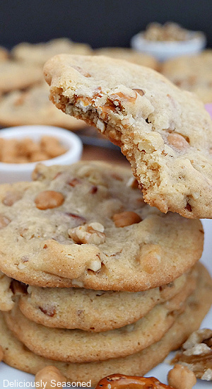 A close up of a cookie with a bite taken out of it and a stack of cookies on a white plate.