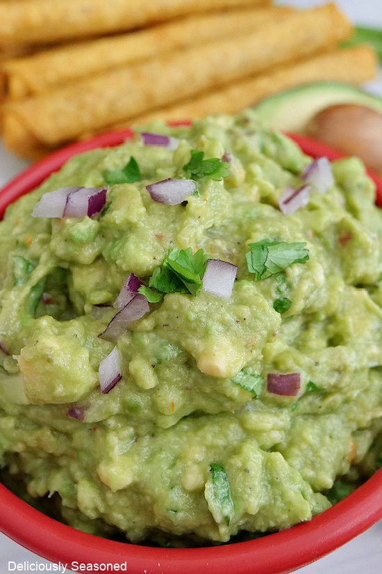 A close up photo of a red bowl filled with easy homemade guacamole.