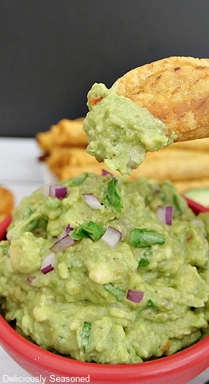 A red bowl filled with homemade guacamole and a close up of a mini taco that has been dipped into the guac.