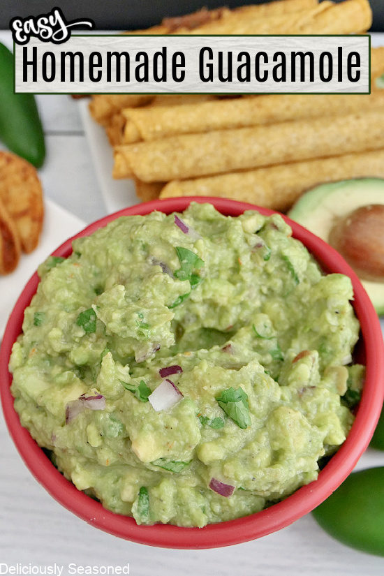 A red bowl with homemade guacamole in it with taquitos in the background.