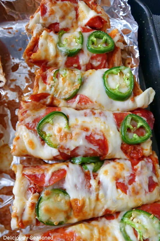 A close up photo of on half of a pepperoni and jalapeno French bread pizza that is placed on a baking sheet covered in foil.