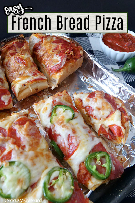 A baking sheet lined with aluminum foil with two sliced French bread pizzas on it.