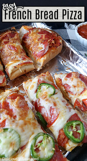 A baking sheet lined with aluminum foil with two sliced French bread pizzas on it.