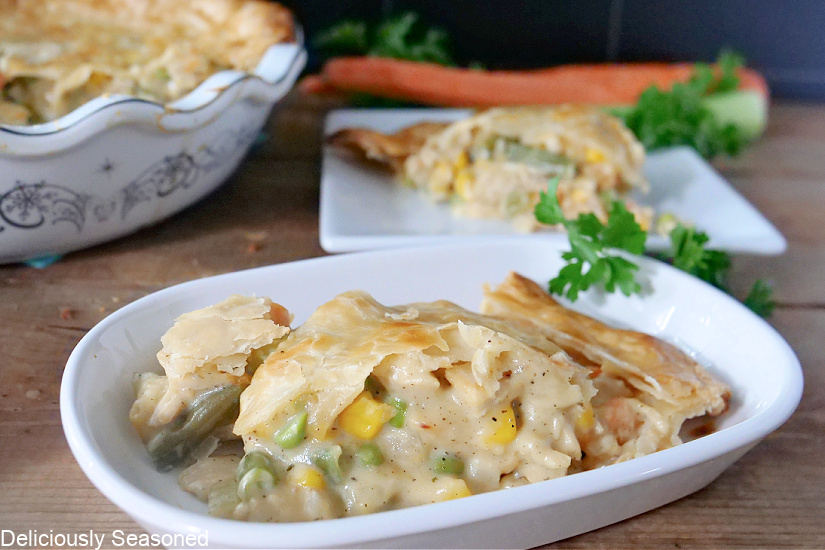A slice of Turkey Pot Pie on a white plate with the pie pan and another plate with pot pie on it in the background.