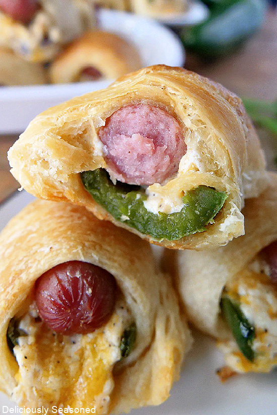 A super close up of a jalapeno popper pigs in a blanket showing the little smokie, jalapeno and cheese blend with a flaky crust.