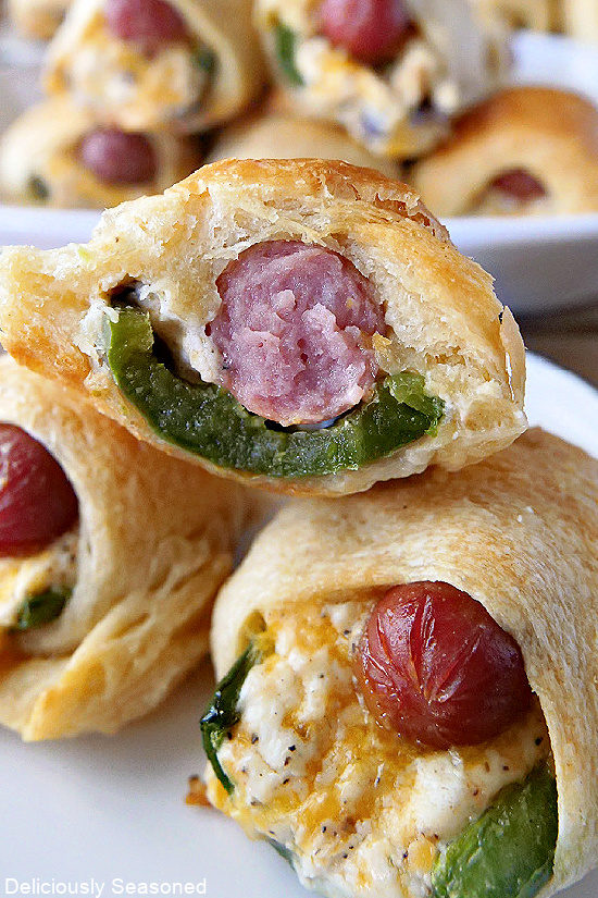 Three jalapeno popper pigs in a blanket on top of each other with a bite taken out of one of them.