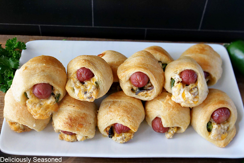 A white plate with 12 jalapeno popper pigs in a blanket on it.