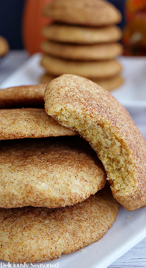 A white plate with a stack of pumpkin snickerdoodles on it and one cookie leaning up along side with a bite taken out of it.