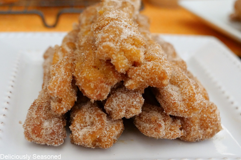 Churros stacked up on a white plate, coated in a cinnamon sugar mixture.