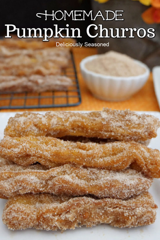 Pumpkin churros stacked up on a white plate with a small white bowl of cinnamon sugar mixture in the background.