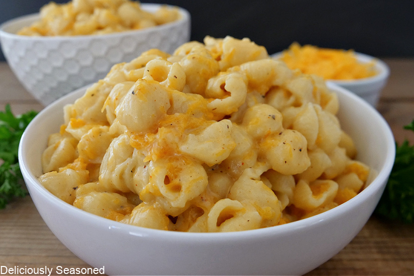 A white bowl filled with mac and cheese with shredded cheese in the background.