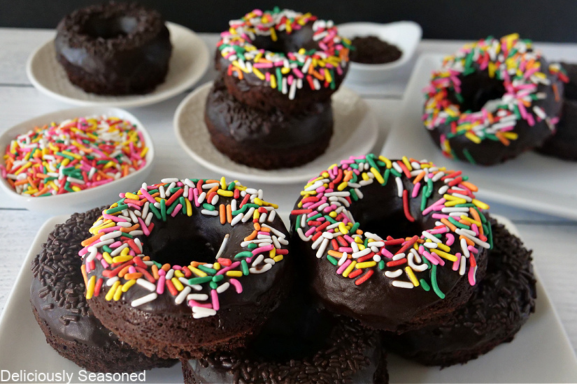 A white board with a stack of chocolate cake donuts on a white plate with more donuts on white plates.