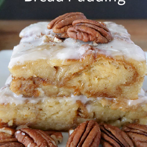 Two slices of bread pudding on top of each other, topped with a glaze, with pecans sitting on top and around the plate.
