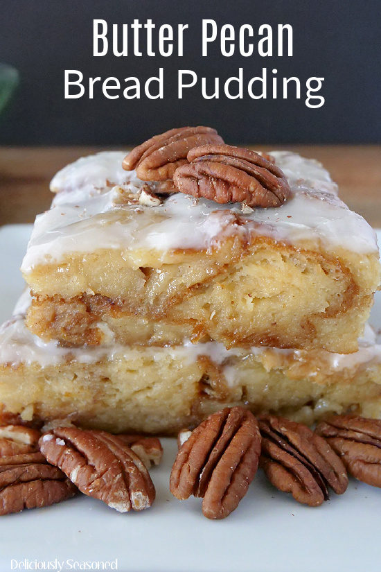 Two slices of bread pudding on top of each other, topped with a glaze, with pecans sitting on top and around the plate.
