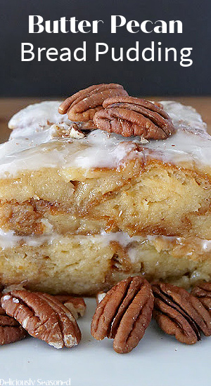 Two slices of bread pudding stacked on top of one another, topped with glaze and pecans.
