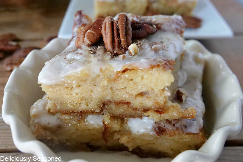 A white dish with a spice of bread pudding in it, topped with glaze and pecans.