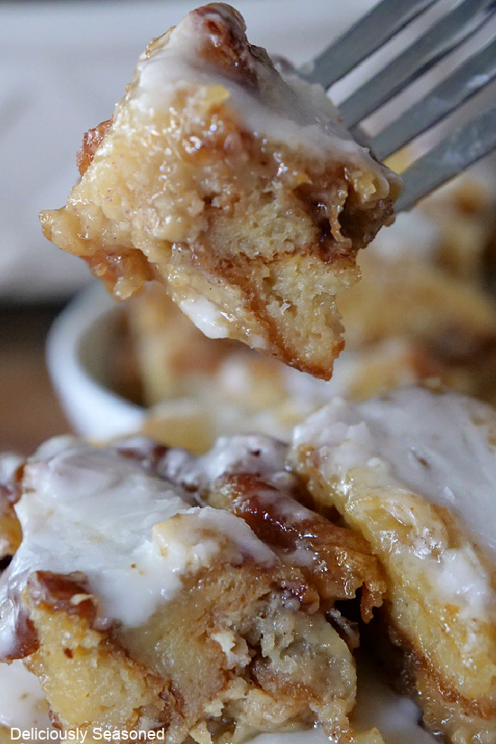 A bite of bread pudding on a fork, sitting above a plate of bread pudding.
