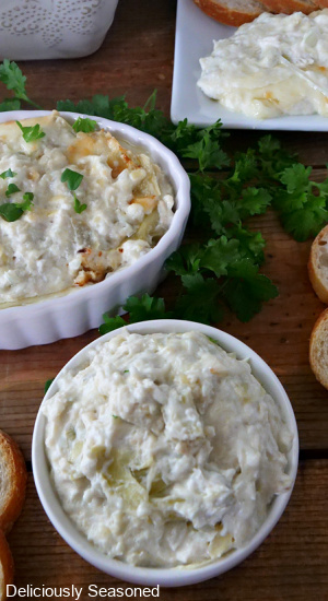 An overhead photo showing bowls filled with artichoke dip, topped with parsley flakes, and slices of bread.