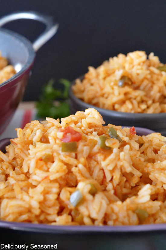A close up photo of Spanish rice stacked high in a bowl with diced tomatoes and jalapenos sitting in the rice.