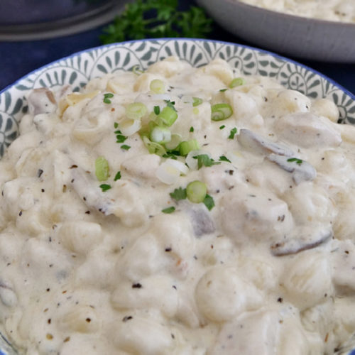 A large bowl of chicken alfredo in a bowl with blue trim.