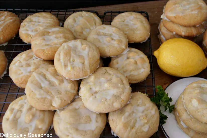 A wire rack filled with lemon cookies and a small white plate with three cookies on it, a lemon and more cookies in the background.