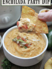A close up of a tortilla chip with cheesy enchilada dip on it.