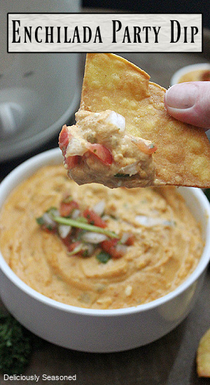 Enchilada party dip in a small bowl with a tortilla chip full of dip and diced tomatoes on top.