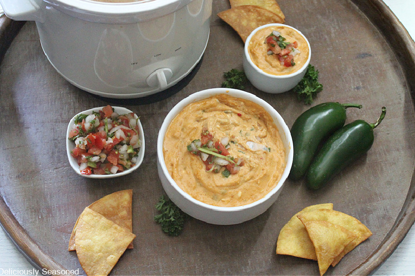 Two small white bowls fill with a cheesy enchilada dip with a small white crock pot in the background.