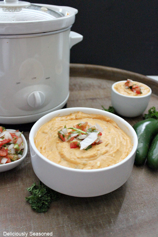 A white bowl filled with a cheesy dip with a white crock pot in the background.