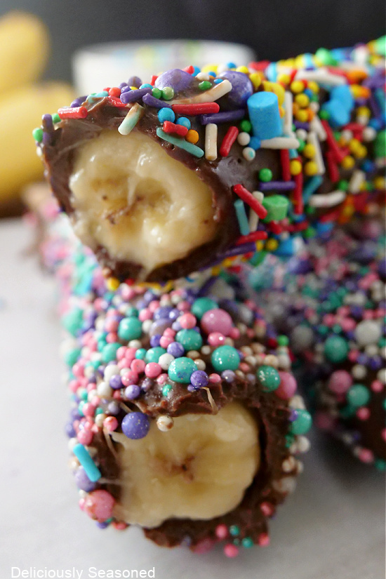 Two chocolate covered bananas with colorful sprinkles on it, with a bite taken out of each.