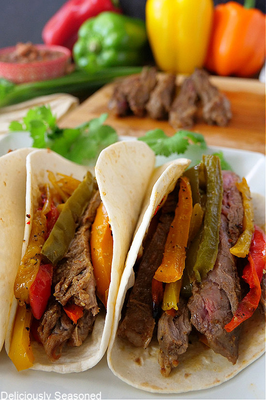 Two steak fajitas on a white plate, filled with bell peppers and onions.