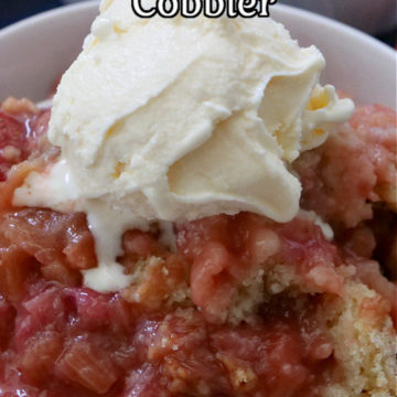 Strawberry rhubarb cobbler in a white bowl, topped with vanilla ice cream.