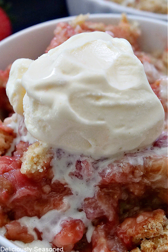 A scoop of melted vanilla ice cream on top of strawberry rhubarb cobbler.