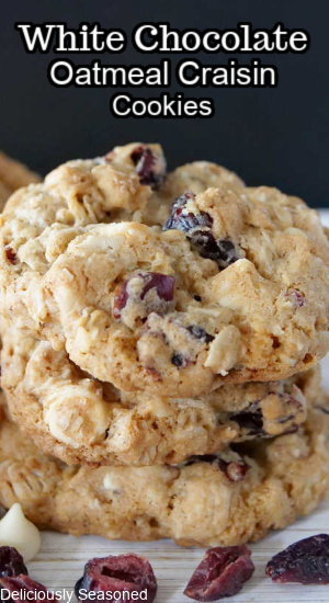 Three cookies stacked up high with craisins and white chocolate chips scattered around in front.