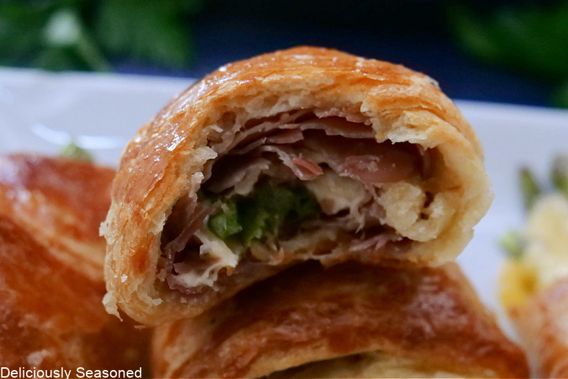 A crescent roll with a bite taken out of it, showing the inside filled with cheese, asparagus, and prosciutto. 
