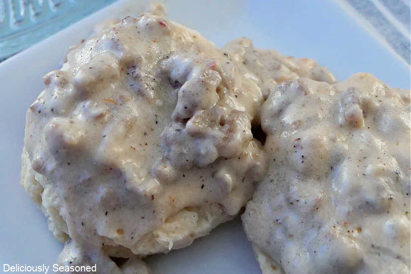 A close up photo of two homemade biscuits with sausage gravy poured over them.
