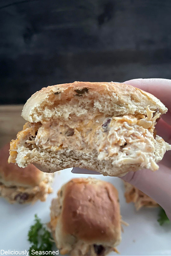 A mini chicken sandwich with a bite taken out of it showing the filling in-between a small bun. 