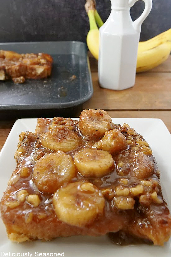 A slice of french toast on a white plate, topped with chopped walnuts and sliced bananas.