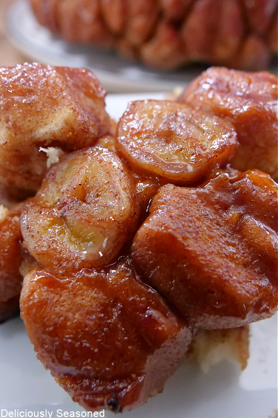 A close up photo of a piece of monkey bread topped with sliced bananas and a sauce on top.