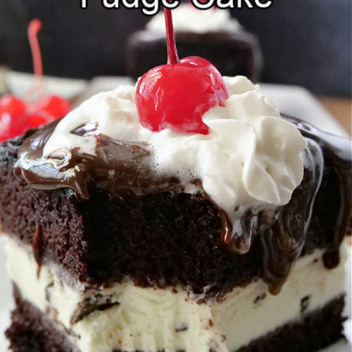 A slice of chocolate cake on a white plate, topped with hot fudge, whipped cream, and a cherry.