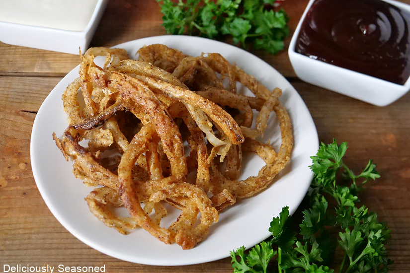 Crispy onion strings on a white plate with BBQ sauce and ranch in small white bowls.